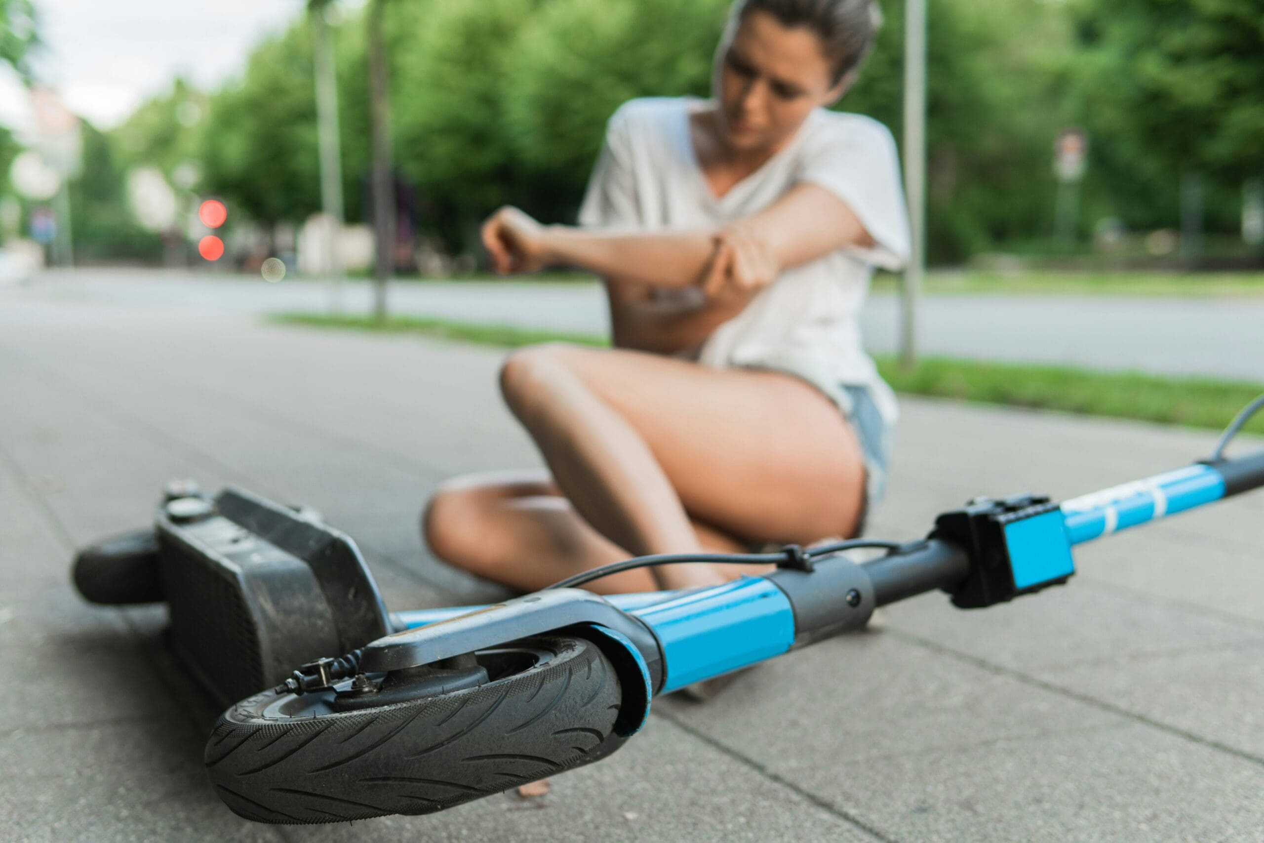 Frau sitzt nach einem Sturz neben einem E-Scooter auf dem Gehweg, unterwegs im Stadtverkehr mit elektrischer Mobilität.
