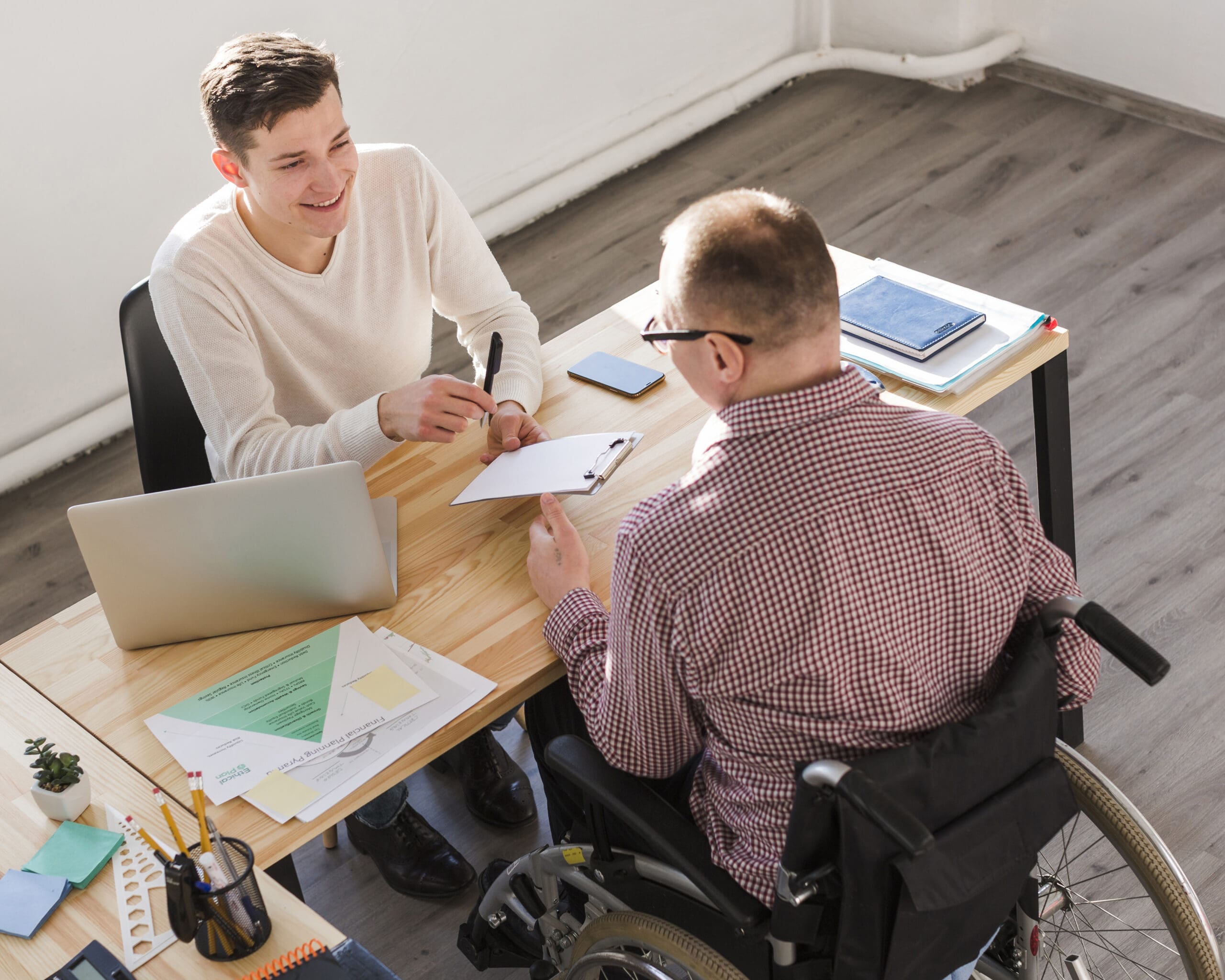 Beratungsgespräch zur Berufsunfähigkeitsversicherung zwischen Berater und Kunde im Rollstuhl zur Absicherung der Arbeitskraft und des Einkommens.